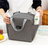 A gray insulated canvas tote bag with double pockets is held by a person on a white surface.