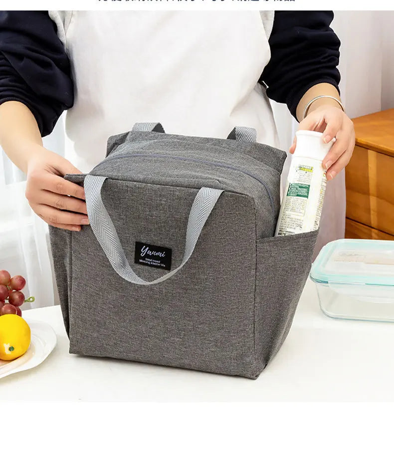 A gray insulated canvas tote bag with double pockets is held by a person on a white surface.