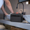 A dark gray travel toiletry organizer bag resting on a white counter next to a sink.