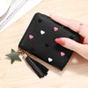 A black PU leather wallet with a zipper closure decorated with small pink and white heart patterns, shown next to a gold tass