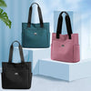 Three nylon shoulder tote bags in teal, pink, and black displayed on white pedestals.