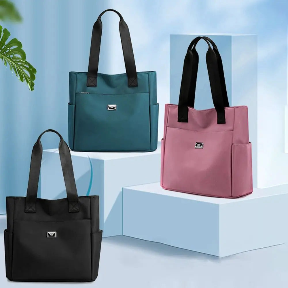Three nylon shoulder tote bags in teal, pink, and black displayed on white pedestals.