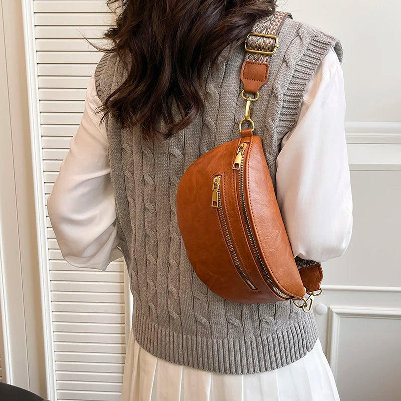 A woman wears a gray knitted vest over a white shirt, carrying a tan leather crossbody bag.