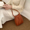 A woman holds a pleated brown PU leather crossbody bag while sitting on a floor.