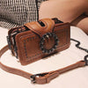 A brown PU leather crossbody bag with a studded design and a rhinestone buckle resting on a white surface.