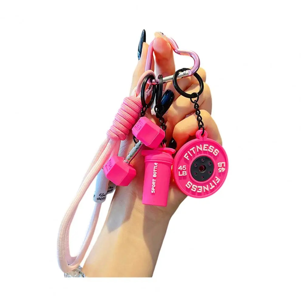 A hand holds a pink fitness keychain featuring charms of a dumbbell and kettlebell.