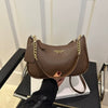A brown leather crescent crossbody bag with gold chain details resting on a black surface.