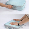 A hand is opening a light blue fabric travel organizer bag, showing its vertical design and storage features.