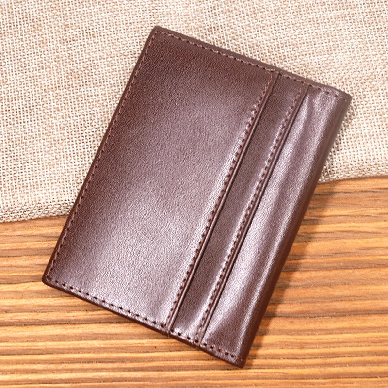 A dark brown genuine leather bifold card holder resting on a wooden surface.