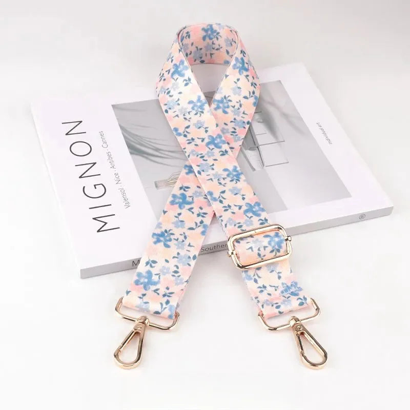 A light blue floral patterned diagonal shoulder strap for bags displayed next to a product box.