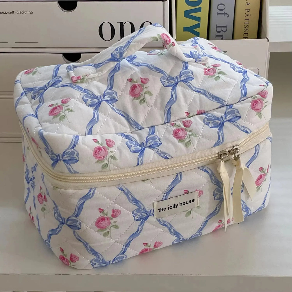 A quilted white makeup bag with blue ribbon embroidery and pink floral accents.