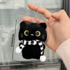 Un dije o llavero de gato negro de peluche sostenido en una mano, mostrando su tamaño y detalle.