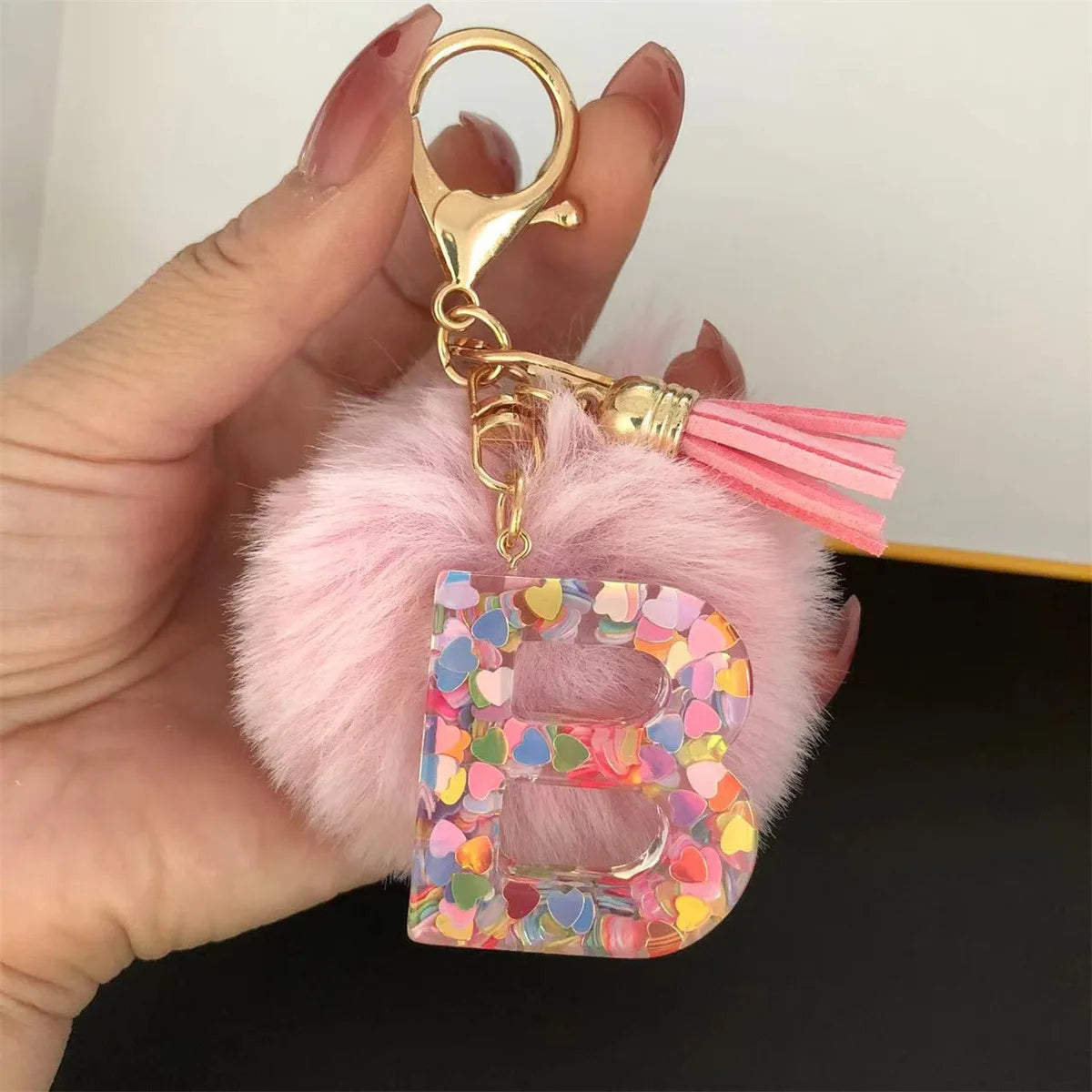 A hand holds a custom initial letter keychain featuring a shiny resin pendant and pink alphabet charm.
