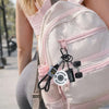 A light pink backpack features a detachable dumbbell keychain charm attached to the zipper.