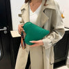 Una mujer sostiene un bolso de monedas con forma de corazón verde contra un abrigo beige claro.