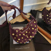 A dark purple faux suede hobo crossbody bag with gold rivet accents displayed on a wooden surface.