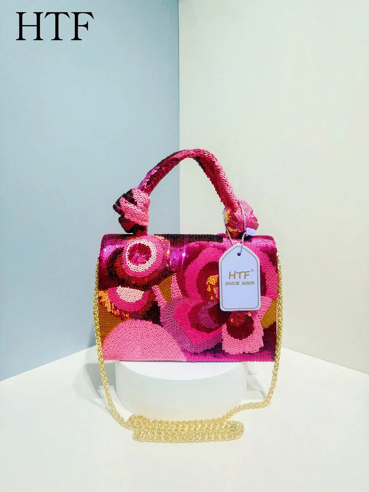 A pink and magenta sequin embroidered floral clutch bag with a gold chain strap displayed on a white surface.