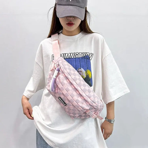 A person is holding a pink plaid crossbody chest bag with an adjustable strap against a white shirt.
