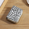 A compact wallet with a leopard print design in white and black spots resting on a wooden surface.