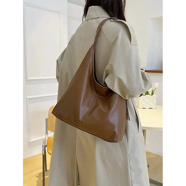 A woman is shown from behind wearing a beige trench coat and carrying a brown PU leather slouchy hobo shoulder bag.