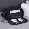 A black PU leather travel toiletry bag with organizer pockets and a brush is shown on a gray surface.