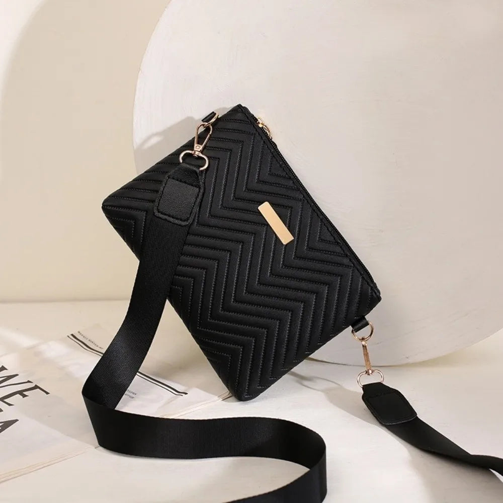 A black quilted chain crossbody bag with gold hardware resting on a white surface.