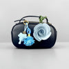 A black PU leather bag with a green cord strap and a light blue floral rosette charm attached.
