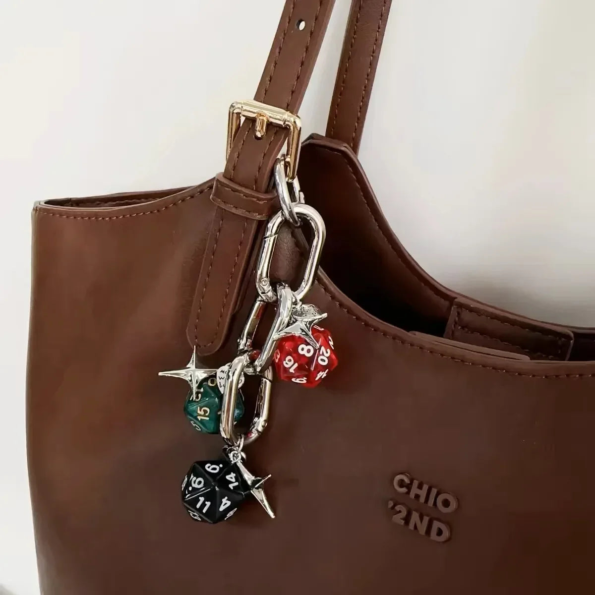 A brown leather handbag with a gold-toned chain keychain featuring resin dice in red, green, and black.
