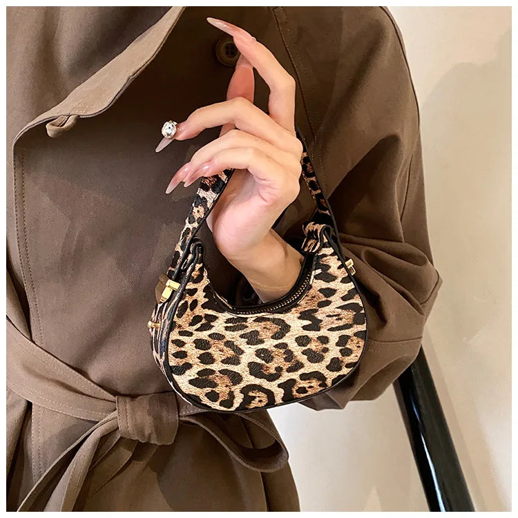 A close-up shot of a woman holding a leopard print PU leather mini tote handbag against a brown blazer.