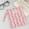 A pink and white floral plaid cotton tablet pouch with a red ribbon closure resting on a white surface.