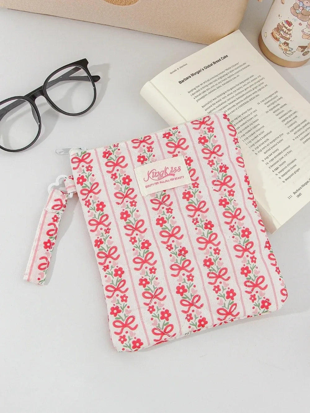 A pink and white floral plaid cotton tablet pouch with a red ribbon closure resting on a white surface.