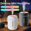 A white desktop mini humidifier with colorful ambient lights is shown on a wooden surface.