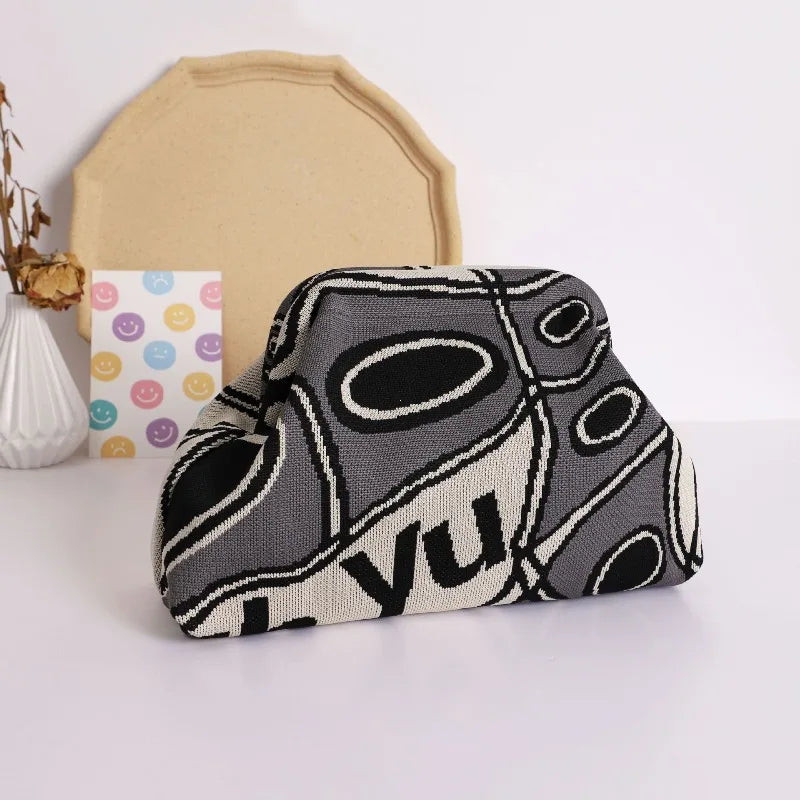 A close-up of a trendy knitted clip bag featuring a black and white abstract pattern resting on a white surface.