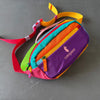 A colorful patchwork color block fanny pack with a pink strap lying on a gray surface.