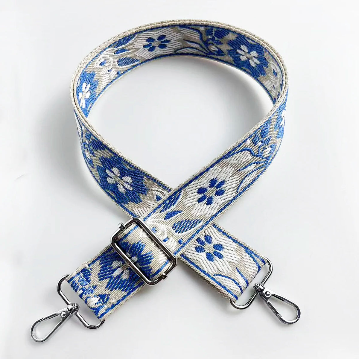 A blue and white floral jacquard strap for a crossbody bag, featuring a silver buckle.