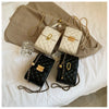 A collection of quilted leather crossbody bags in cream and black with gold metal straps resting on a beige fabric.