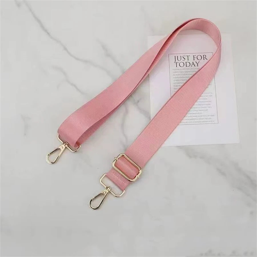 A pink nylon shoulder strap with gold hardware is displayed on a white marble surface.