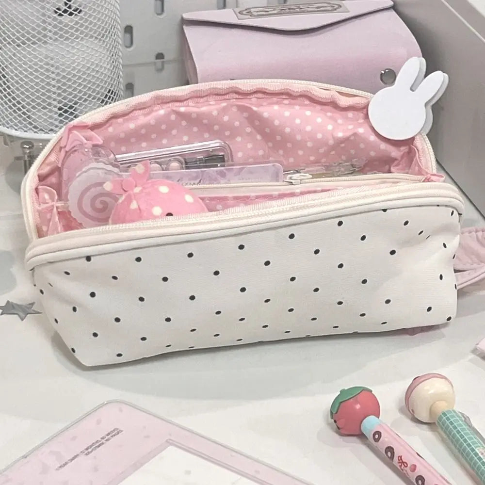 A pink and white polka dot shell pencil case with a zippered interior and a matching pink cosmetic pouch.