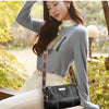A woman models a black luxury cowhide shoulder bag while wearing a gray turtleneck sweater and white pants outdoors.