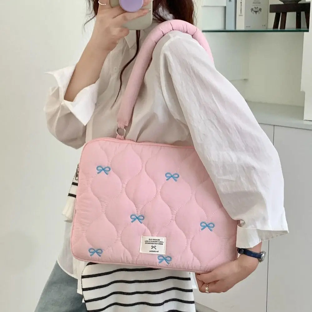 Bolso de portátil acolchado rosa con detalles de lazo azul llevado por una persona.