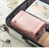A pink portable makeup bag with a leather trim is shown inside an open travel case.