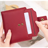 A hand holds a maroon RFID blocking bi-fold card holder wallet with a clear plastic slot.