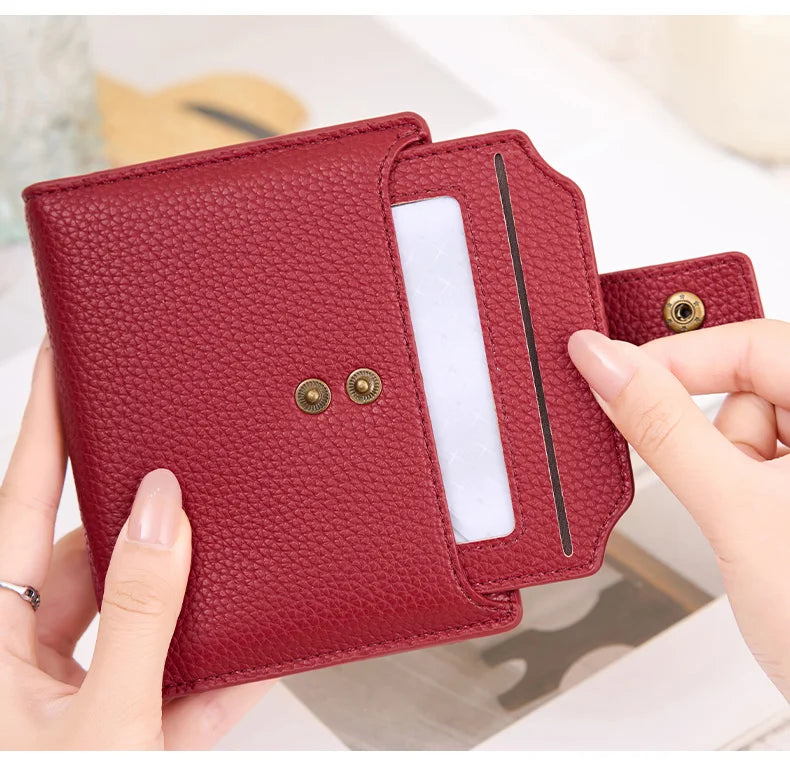 A hand holds a maroon RFID blocking bi-fold card holder wallet with a clear plastic slot.
