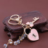 Gold and pink rhinestone key chain featuring a bow and heart charm resting on dark wood.