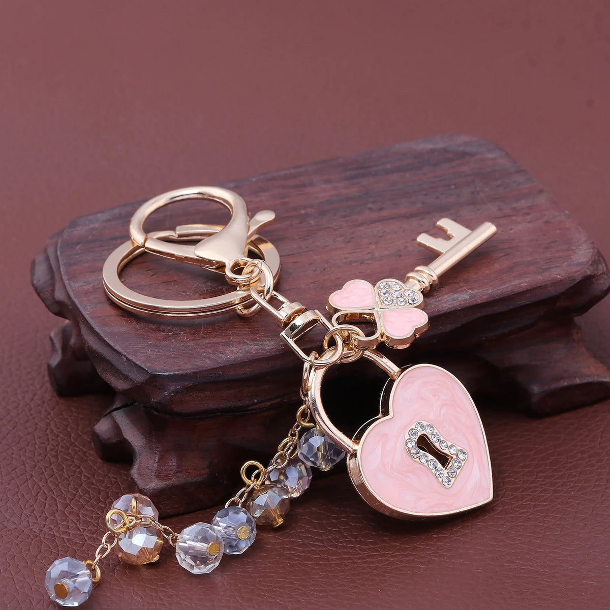 Gold and pink rhinestone key chain featuring a bow and heart charm resting on dark wood.