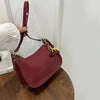 A maroon PU leather shoulder bag with a strap and gold cherry pendants is being held by a hand.