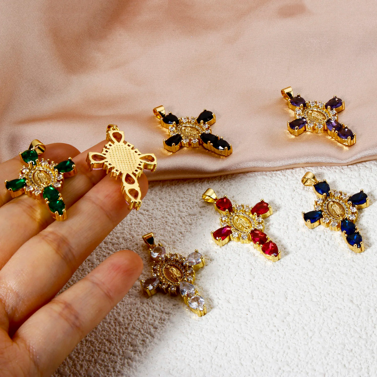 A hand holds several gold-plated cross and Virgin Mary charm pendants adorned with cubic zirconia stones.
