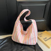 A pink and white striped canvas shoulder bag with a curved handle resting on a black leather jacket.