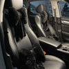 Interior view of a car seat showing a black leather seat with fuzzy bowknot headrest pillows and lumbar support.