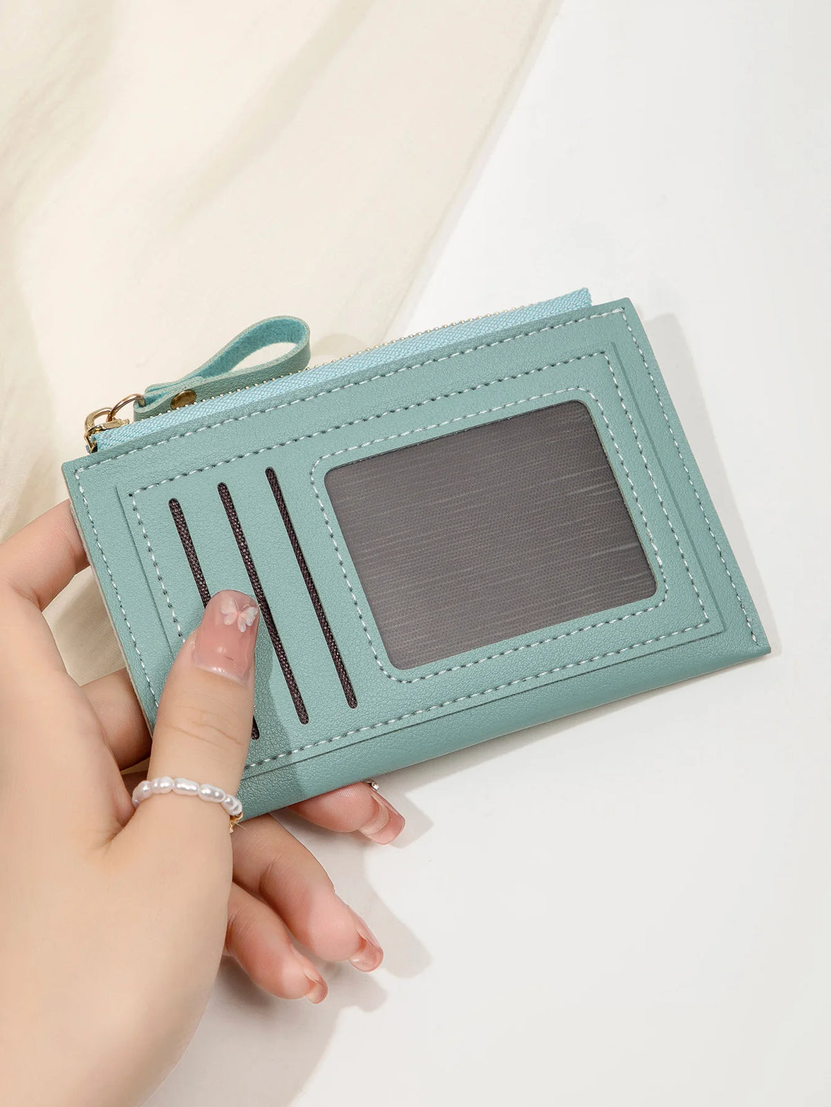 Une main tient un portefeuille en cuir PU vert menthe minimaliste avec une fenêtre en plastique transparent et des fentes ver